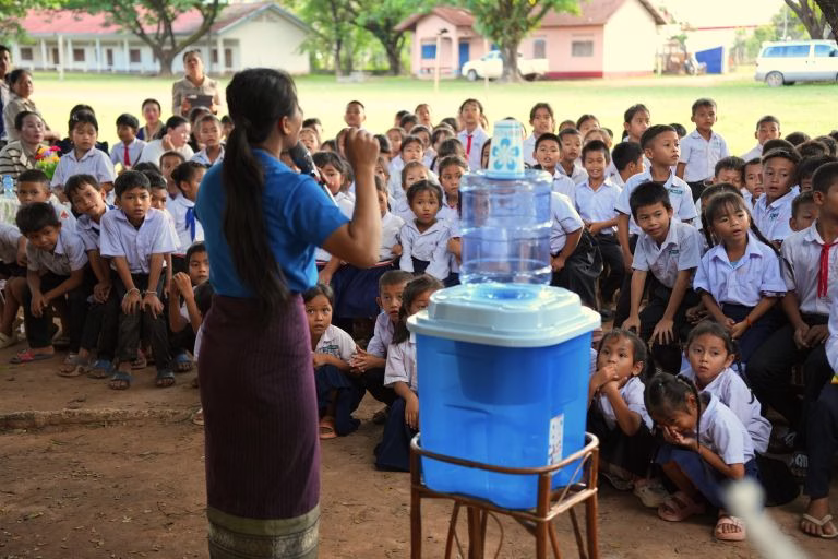 TerraKids employee, holding TerraKids learning materials in front of large gathering of students outside a school